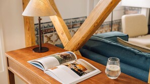 A wooden bedside table with a lamp, a book, a glass of water, and a blue sofa in the background.