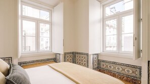 A bedroom with a bed, two windows, and patterned tile borders.