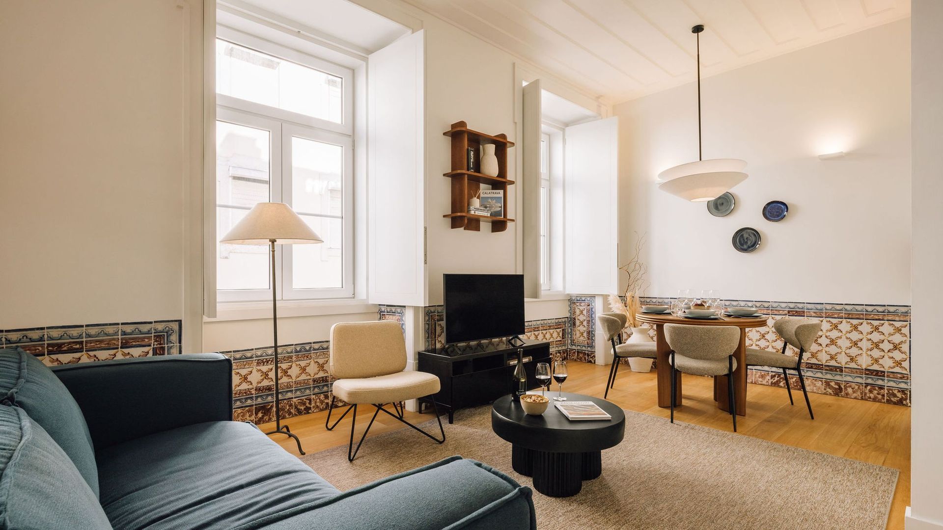 Ein Wohnzimmer mit einer Couch, Sesseln, einem Couchtisch, einem Fernseher und einem Essbereich mit Tisch und Stühlen.