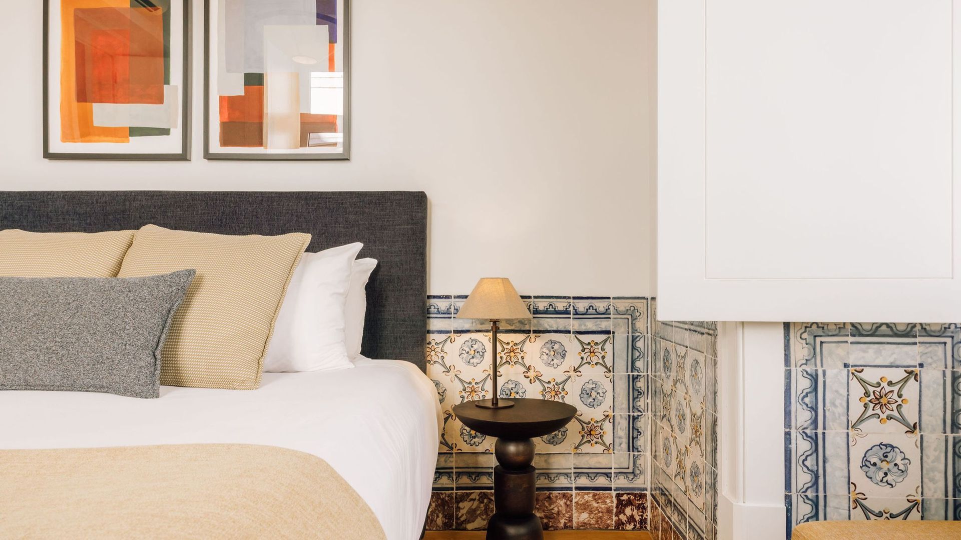 Een net opgemaakt bed met meerdere kussens, een bedlampje en een decoratief patroon op de wandtegels.