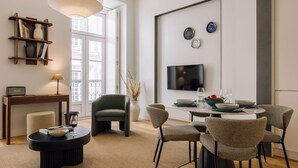 A modern living room with a dining area, featuring a sofa, chairs, a table, a bookshelf, and a TV. - Ando Living - São Nicolau House - 301 (Lisboa)
