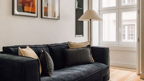 Ein dunkelgraues Sofa mit mehreren Kissen, eine Stehlampe und gerahmte Bilder an der Wand.