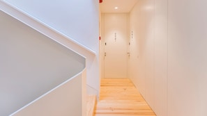 A narrow hallway with wooden flooring and white walls. There are doors with numbers on them.