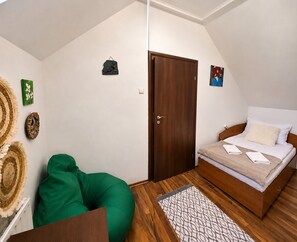 A bedroom with a bed, a green chair, a wooden door, and a small artwork on the wall.