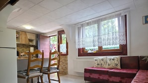 Un espacio habitable compacto con kitchenette, un comedor con sillas de madera, un sofá con cojines estampados y un ventanal con cortinas de encaje.
