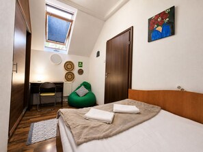 A bedroom with a bed, a desk, a chair, a window, and a door.