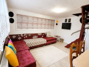 A living room with a sofa, a small round table, a TV mounted on the wall, and a staircase.