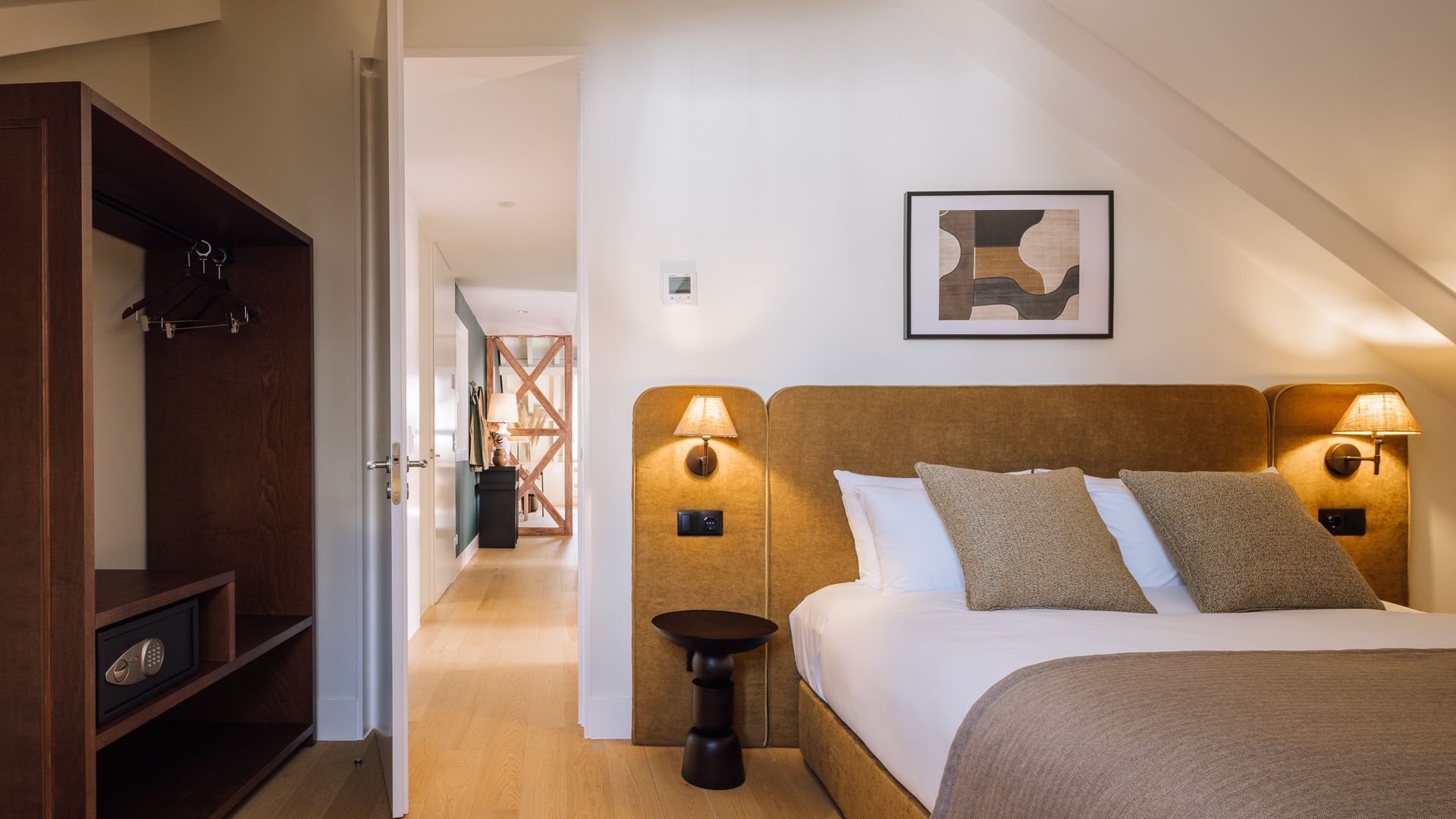 Une chambre à coucher comprenant un lit, des lampes de chevet, une tête de lit, une œuvre d’art accrochée au mur et une armoire.
