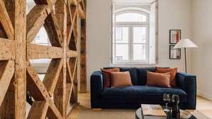 Ein Wohnzimmer mit einem dunkelblauen Sofa, Holzbalken, einem Fenster und einer Stehlampe.