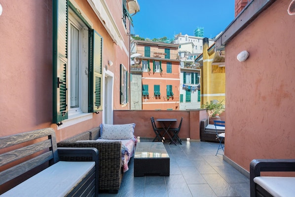 A narrow outdoor patio with wicker furniture, a small table, and a view of adjacent buildings.
