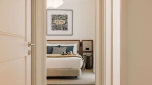 Una habitación de hotel con cama, mesita de noche, una obra de arte abstracta enmarcada y una puerta que da a otra estancia.
