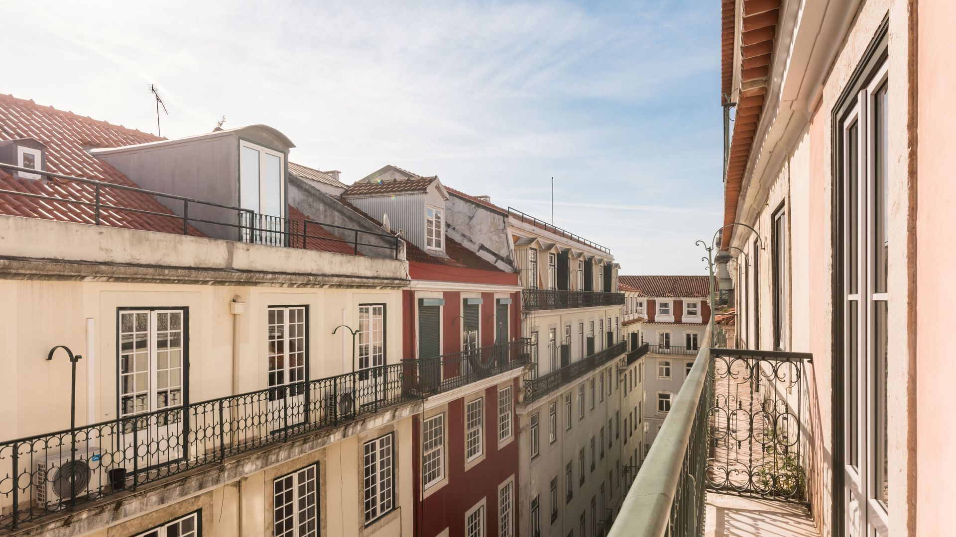 A narrow street with buildings on either side, featuring balconies and a clear sky.