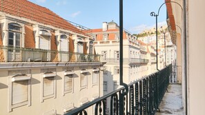 A row of historic buildings with red-tiled roofs and balconies, a metal railing, and a clear sky. - Ando Living - Santa Justa 79 House - 401 (Lisboa)