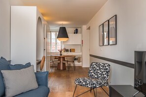 A modern living room with a sofa, a patterned chair, a dining area with a table and chairs, and a kitchen in the background. - Ando Living - Santa Justa 77 House - 501 (Lisboa)