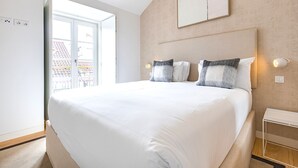 A hotel room with a large bed, a window with a view, a bedside table, and a wall-mounted light. - Ando Living - Douradores House - 503 (Lisboa)
