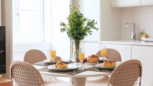 A breakfast setting with a table, chairs, a vase with flowers, and plates with croissants and juice glasses. - Ando Living - Douradores House - 503 (Lisboa)