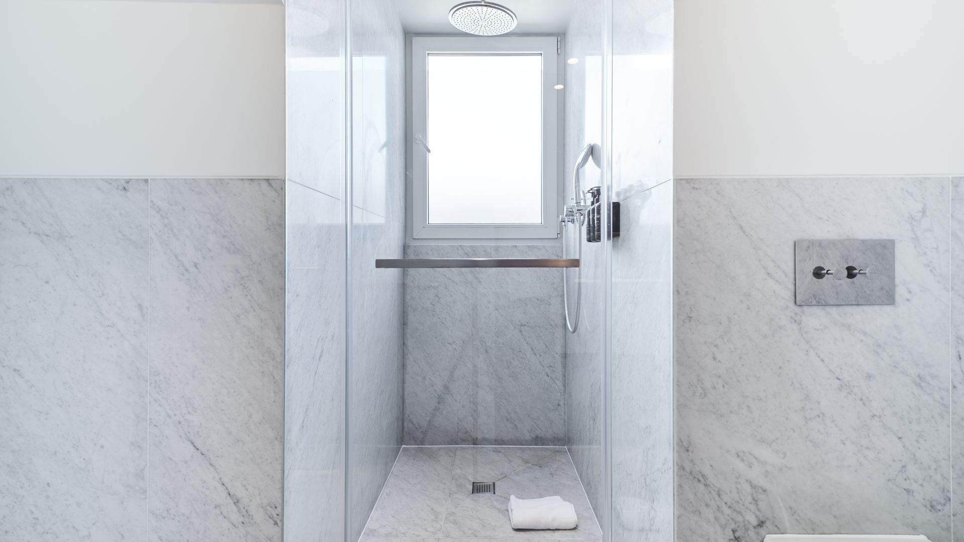 Une salle de bain moderne avec une douche à parois de verre, un porte-serviettes et un interrupteur visible sur le mur.