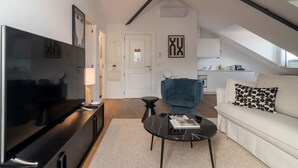Een moderne woonkamer met een flatscreen televisie, een blauwe fauteuil, een witte bank en een salontafel.