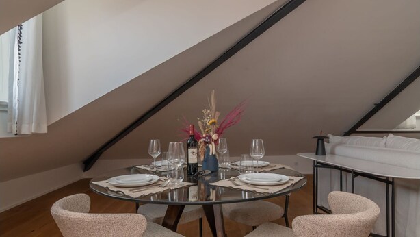 Een eethoek met een glazen tafel, zes stoelen en een vaas met bloemen.