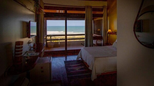 Quarto de hotel com cama, escrivaninha, cadeira, televisão e vista para a praia.