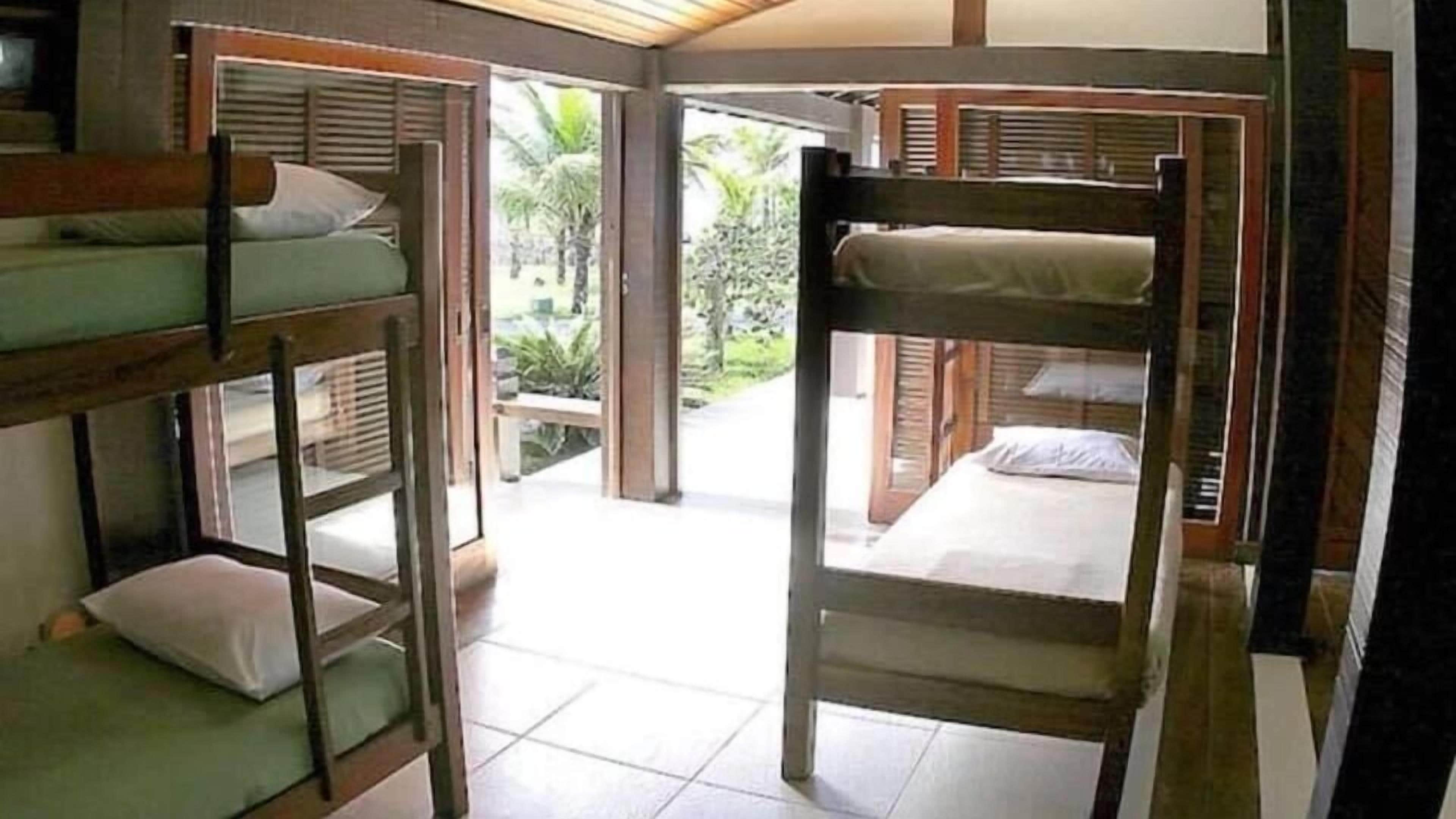 A dormitory-style room with bunk beds, a tiled floor, and a view of a garden through an open door.