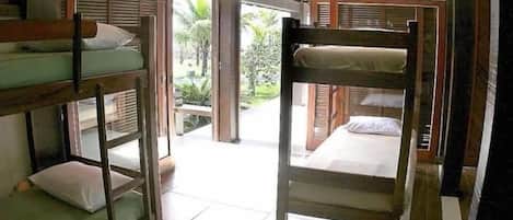 Habitación tipo dormitorio con literas, piso de baldosas y vista a un jardín a través de una puerta abierta.