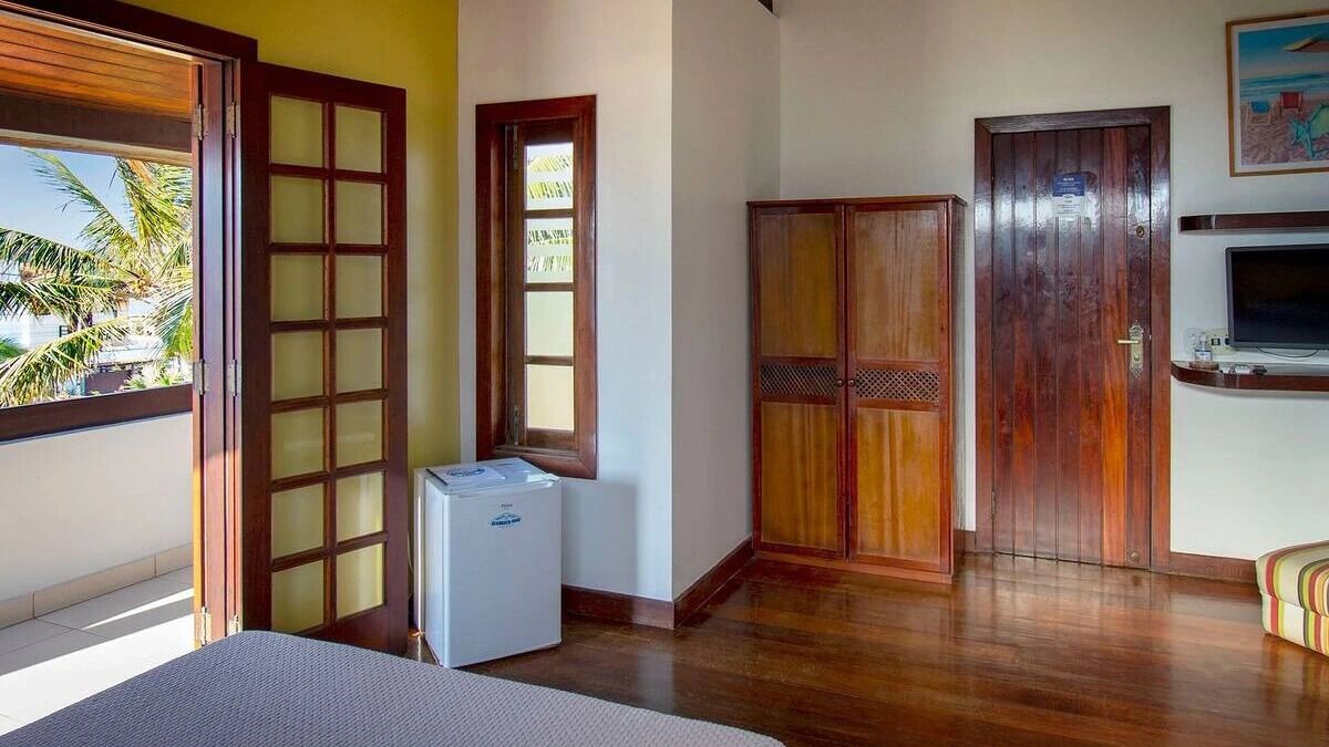 Una habitación con una cama, un refrigerador pequeño, un armario de madera y un televisor en la pared.