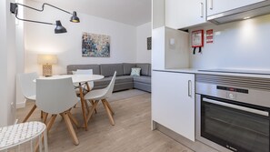 Una cocina moderna con horno Bosch, una zona de comedor con mesa redonda y sillas, y un sofá gris.