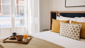 A neatly made bed with a tray of breakfast, including cereal, fruit, and juice, in a room with a view of a balcony. - Abrantes 50 House - One Bedroom Superior City View (Lisbon)