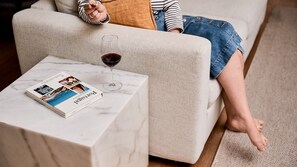 Une personne assise sur un canapé, avec un magazine et un verre de vin rouge posé sur une petite table d’appoint en marbre.