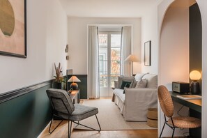 Uma sala de estar moderna com um sofá, cadeiras e uma mesa. Há uma janela com cortinas, um abajur e um quadro na parede.