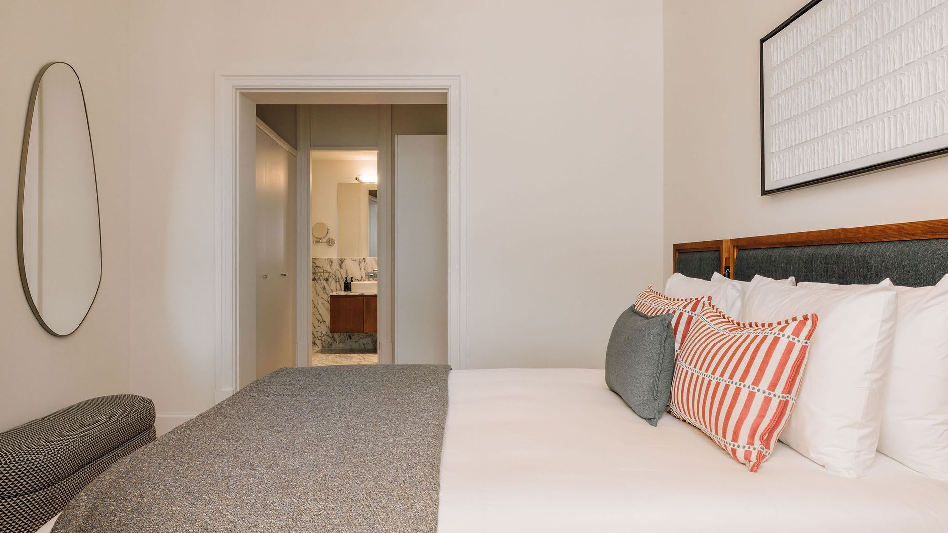 A hotel room with a bed, a chair, a mirror, and a door leading to a bathroom.