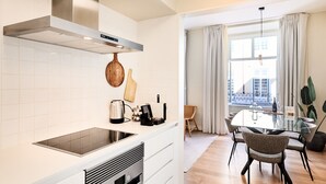Uma cozinha moderna com fogão embutido, chaleira e máquina de café. Há um espaço de jantar com mesa de vidro e cadeiras.