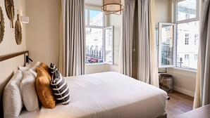 Quarto de hotel com uma cama grande, vista da cidade pela janela e luminária pendente.
