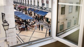 An outdoor café with tables and umbrellas, surrounded by buildings with balconies and signage. - Ando Living - Augusta House - 202 (Lisboa)