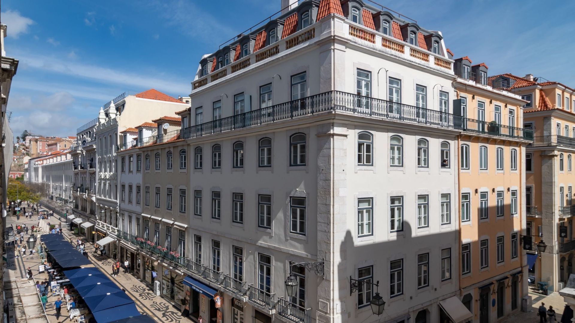 A multi-story building with balconies, large windows, and a street in front.