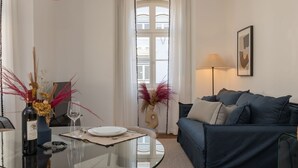 Una sala de estar moderna con una mesa de vidrio, un sofá azul oscuro y un florero con plantas secas.