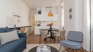 Ein modernes Wohnzimmer mit Sofa, einem Esstisch mit Stühlen, einer Küchenzeile und einer Pendelleuchte.