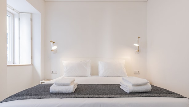 Ein schlicht eingerichtetes Hotelzimmer mit einem großen Bett, zwei Nachttischlampen und einem Fenster, das für natürliches Licht sorgt.