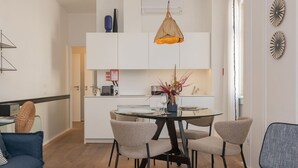 Un salon moderne avec une table à manger en verre, quatre chaises, un canapé et un luminaire suspendu.
