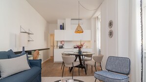Un salon moderne avec un canapé bleu, un fauteuil gris, une table basse ronde et un coin repas comprenant une table et des chaises blanches.