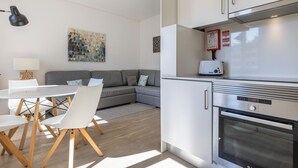 A modern kitchen with a built-in oven and a toaster. There is a dining area with a white table and chairs. - Garcia 28 | Apartment 1B by LovelyStay (Lisboa)