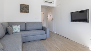 A modern living room with a grey sofa, a flat-screen TV mounted on the wall, and a wooden floor. - Garcia 28 | Apartment 1B by LovelyStay (Lisboa)
