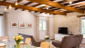 Ein Zimmer mit Esstisch für vier Personen, zwei Sofas, einem Fernseher auf einem Schrank und Steinwänden.