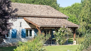 Ein Haus aus Stein mit Ziegeldach, einer Veranda und einem Garten mit verschiedenen Pflanzen und Blumen.