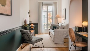 A modern living room with a sofa, chairs, and a table. There is a window with curtains, a lamp, and a framed picture on the wall. - Ando Living - Santa Justa 77 House - 401 (Lisboa)
