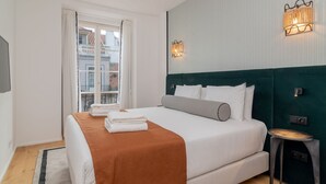 A modern bedroom with a large bed, a view of the city through a window, and two wall-mounted light fixtures. - Ando Living - Santa Justa 77 House - 401 (Lisboa)