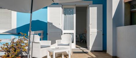 A patio with white wicker furniture, a potted plant, and a white umbrella.