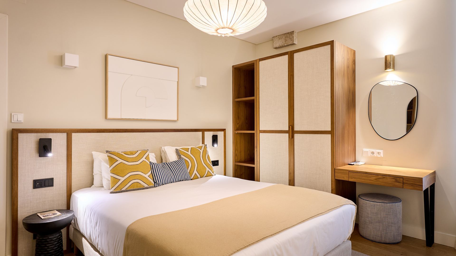 Une chambre d’hôtel avec un grand lit, des tables de chevet, une armoire, un bureau avec un miroir et un luminaire au plafond.