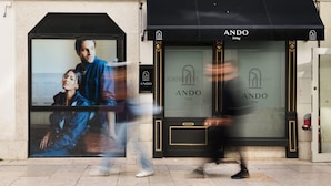 Una vetrina con un grande annuncio che mostra un uomo e una donna. La vetrina ha un tendone nero con il logo "ANDO Living" e un cartello che indica "AUGUSTA TOWERSHED".